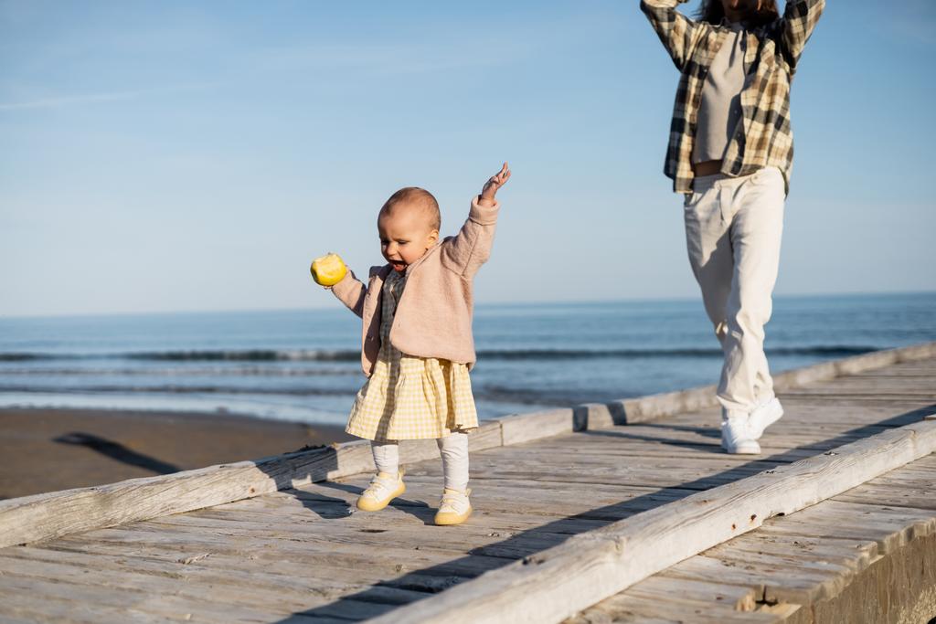 Pikkulapsi tyttö tilalla omena kävellessään laiturilla lähellä isä Italiassa  - Valokuva, kuva