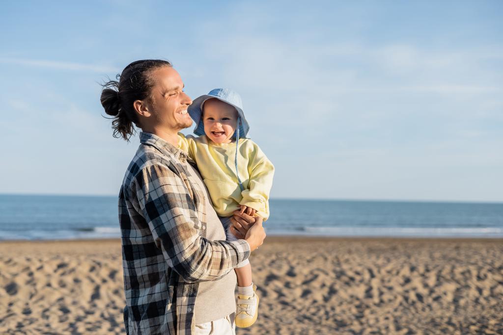 Довговолосий тато тримає веселу дочку на березі біля моря в Італії.  - Фото, зображення
