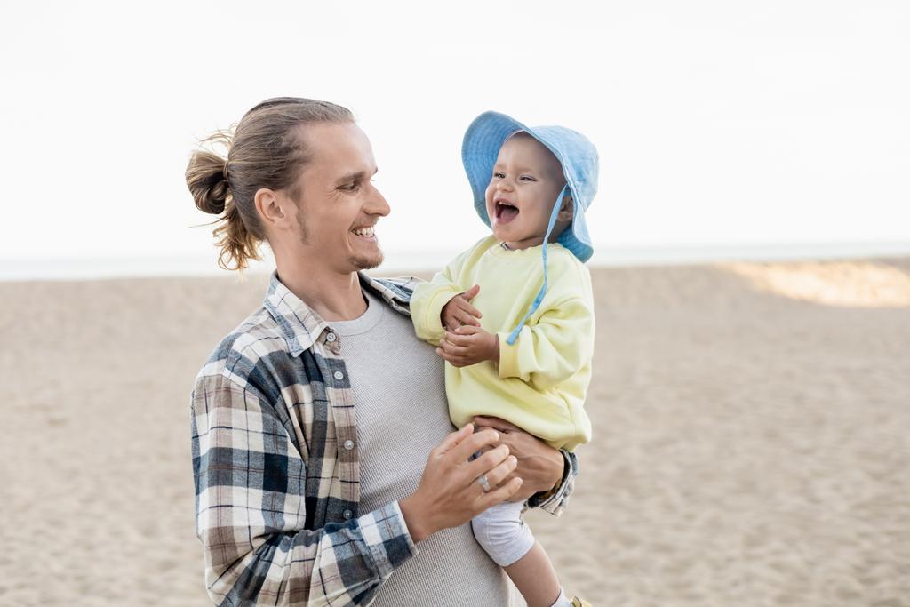 Щасливий батько дивиться, як сміється дитина на пляжі
  - Фото, зображення