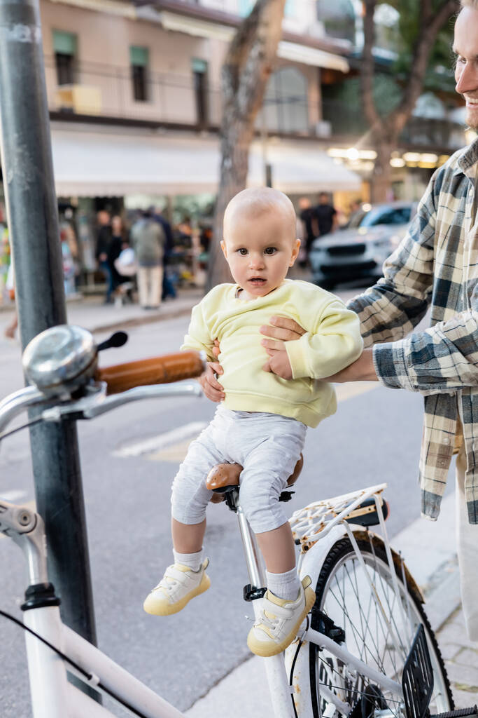 Sonriente padre sosteniendo niña cerca de la bicicleta en la calle urbana en Treviso - Foto, imagen