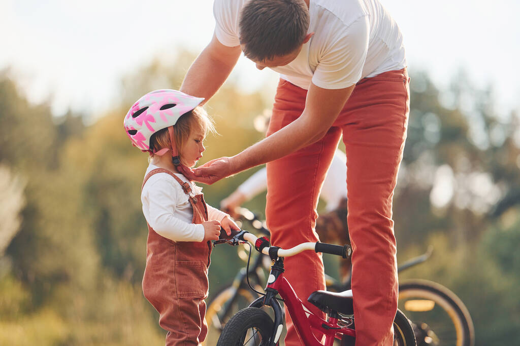 Prachtig zonlicht. Vader in wit shirt leren dochter hoe om te fietsen buiten. - Foto, afbeelding