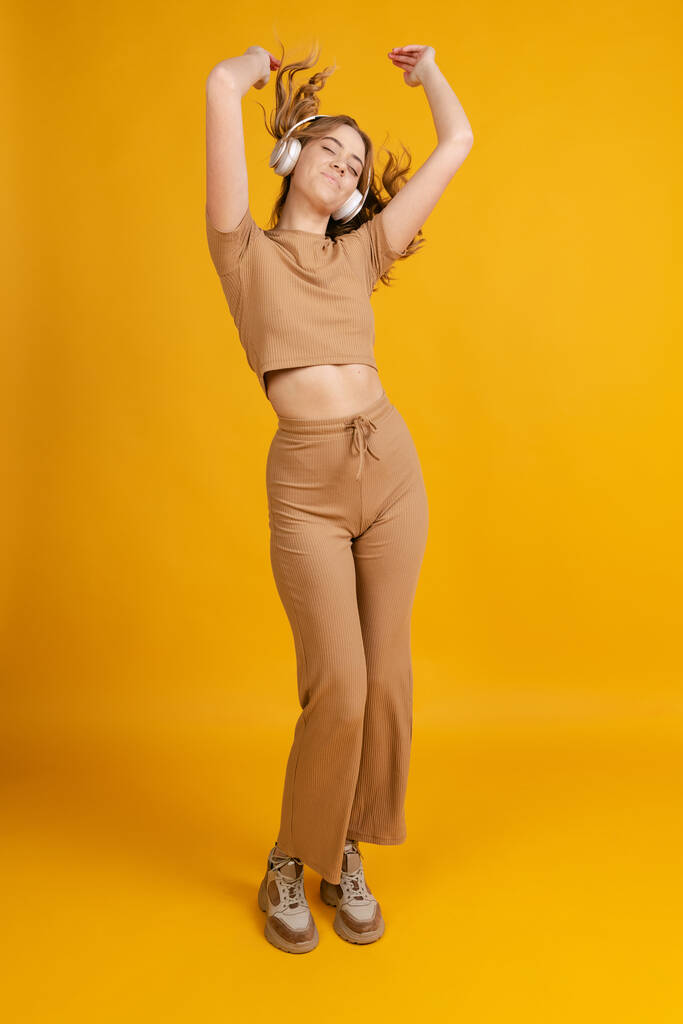 Uma jovem garota emocional, estudante posando, dançando isolada em fundo laranja. Conceito de beleza, arte, moda, juventude, monocromático - Foto, Imagem