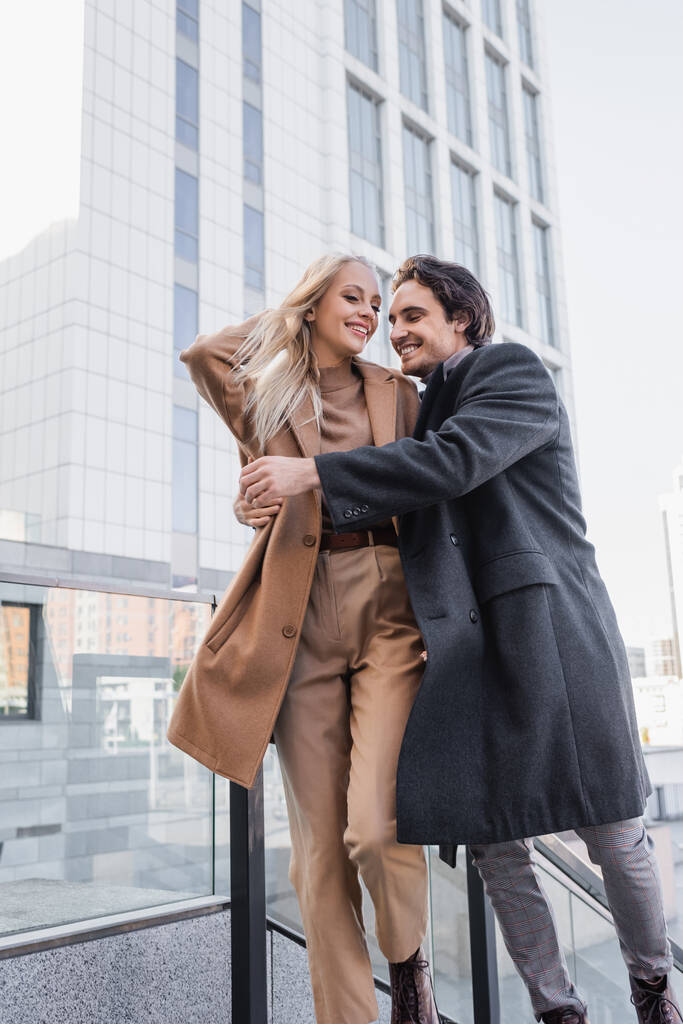 jonge man in jas knuffelen trendy vrouw tijdens het wandelen in de stad - Foto, afbeelding
