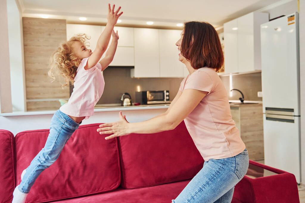 Having fun and jumping. Young mother with her little daughter in casual clothes together indoors at home. - Fotoğraf, Görsel