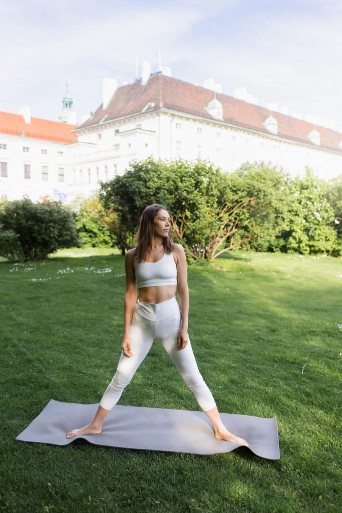 sportive woman in white sports bra and leggings standing in tree pose on yoga mat - Fotoğraf, Görsel