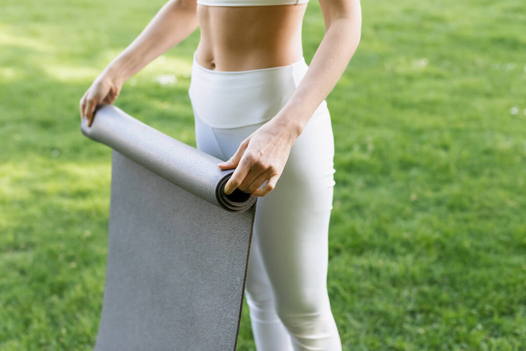 vista ritagliata di donna magra in leggings bianchi tenendo tappeto fitness all'aperto - Foto, immagini