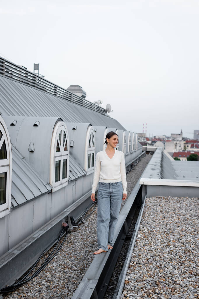 Barfüßige Frau in Jeans läuft auf dem Dach eines städtischen Gebäudes - Foto, Bild