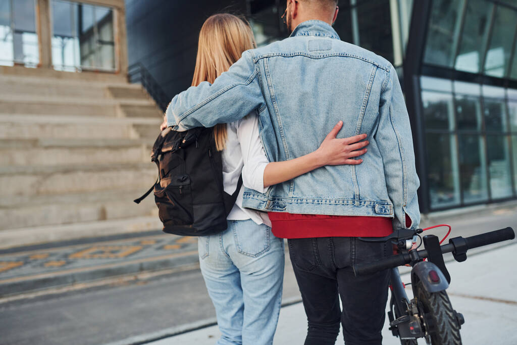 With electric schooter. Young stylish man with woman in casual clothes outdoors near business building together. Conception of friendship or relationships. - Photo, image