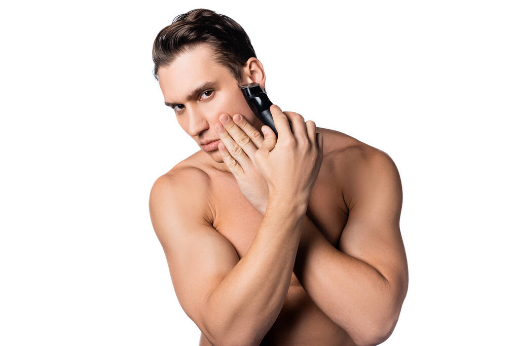 félmeztelen férfi borotválkozás elektromos trimmer, miközben néz kamera elszigetelt fehér - Fotó, kép