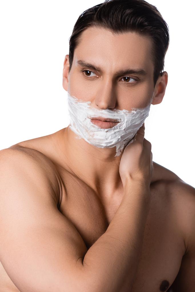 hombre con hombros desnudos y espuma de afeitar en la cara mirando hacia otro lado aislado en blanco - Foto, imagen