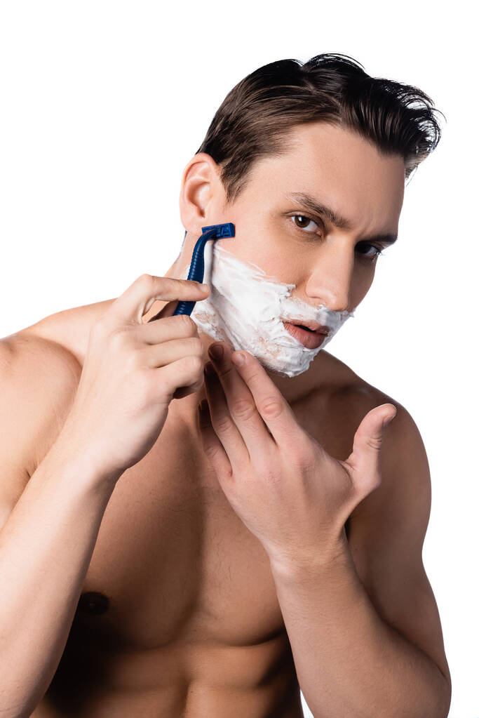 félmeztelen férfi csupasz mellkassal nézi a kamerát és borotválkozás elszigetelt fehér - Fotó, kép