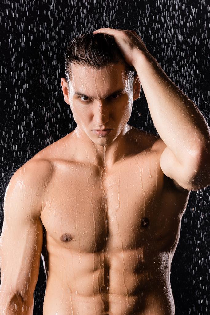 homem confiante olhando para a câmera sob o chuveiro no fundo preto - Foto, Imagem
