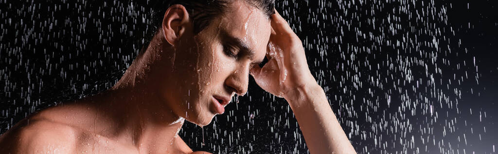 hombre con los ojos cerrados tocando el pelo mientras se ducha sobre fondo negro, pancarta - Foto, Imagen