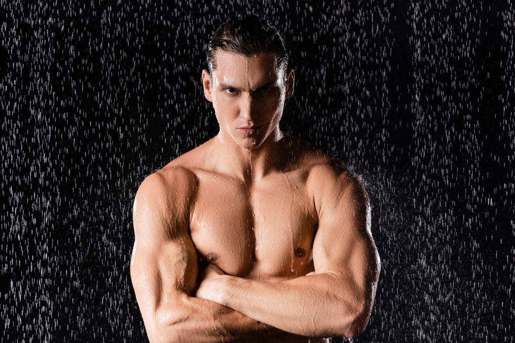 homem confiante com tronco muscular de pé com braços cruzados sob chuva no fundo preto - Foto, Imagem