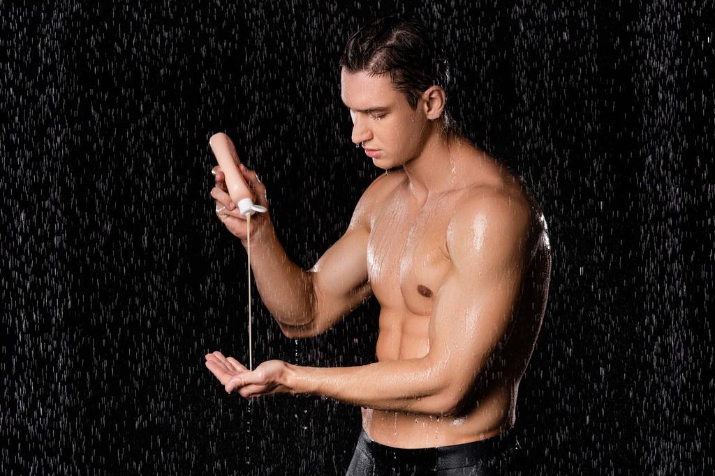 homem molhado com torso muscular segurando gel de chuveiro no fundo preto - Foto, Imagem