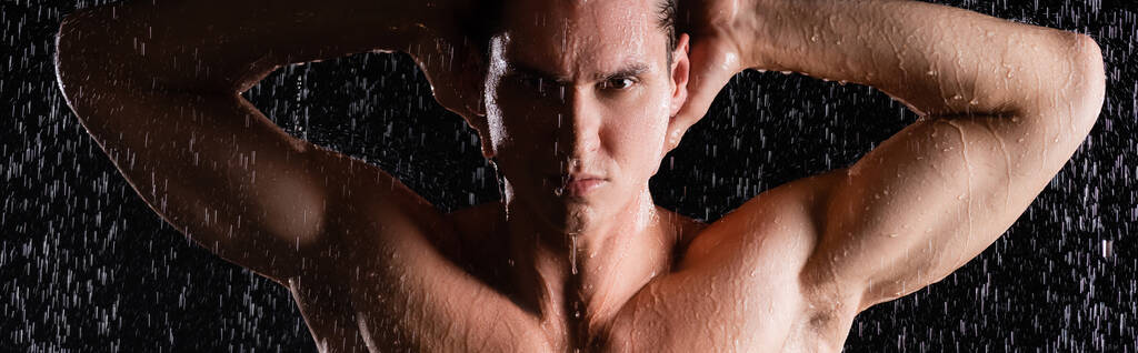 homme musclé posant avec les mains derrière la tête sous la douche sur fond noir, bannière - Photo, image