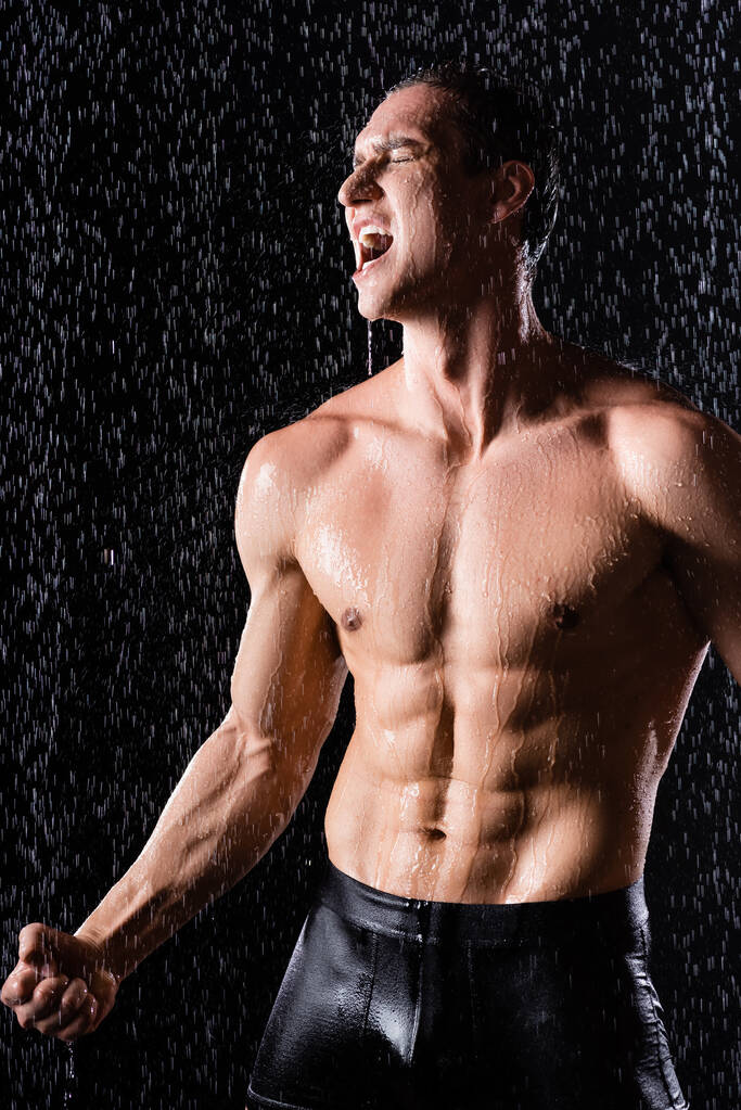 Δυνατός άντρας με σώβρακα να τραγουδάει κάτω από βροχή σε μαύρο φόντο - Φωτογραφία, εικόνα
