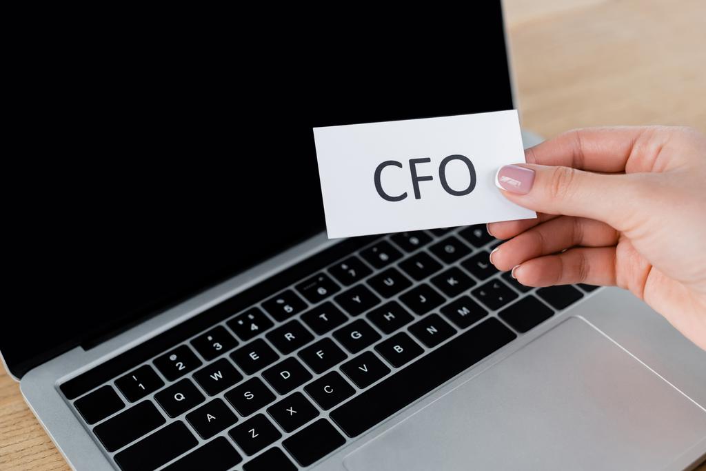 обрезанный вид деловой женщины, держащей бумагу с надписью CFO рядом с ноутбуком  - Фото, изображение