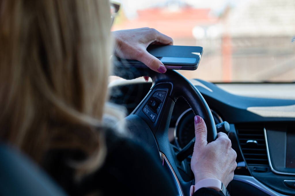 Visão de perto das mãos da mulher com o smartphone segurando o volante - Foto, Imagem