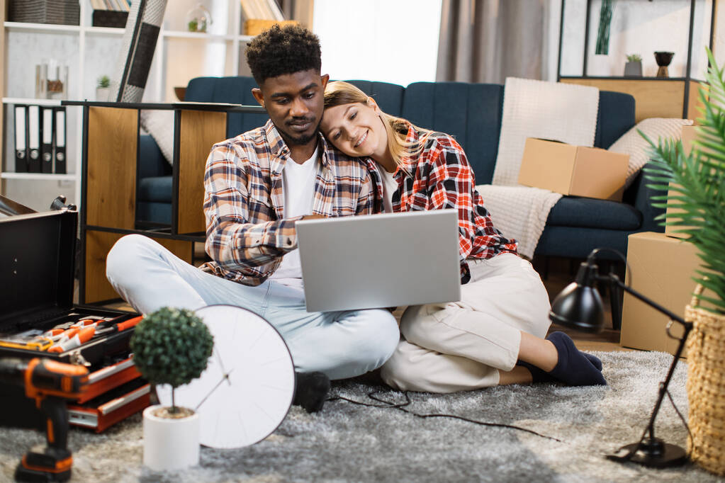 Multiethnisches Paar nutzt Laptop in neuer Wohnung - Foto, Bild