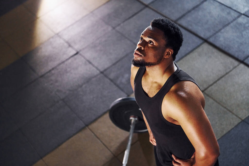 Vue de dessus. Barbell par terre. Homme afro-américain fort en vêtements de sport ont séance d'entraînement journée dans la salle de gym. - Photo, image