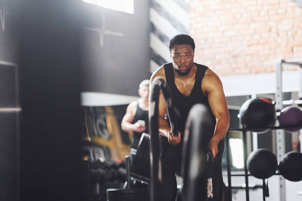 Güçlü Afro-Amerikan spor elbiseli adam spor salonunda antrenman yapıyor. Halat kullanarak Crossfit yapıyor. - Fotoğraf, Görsel