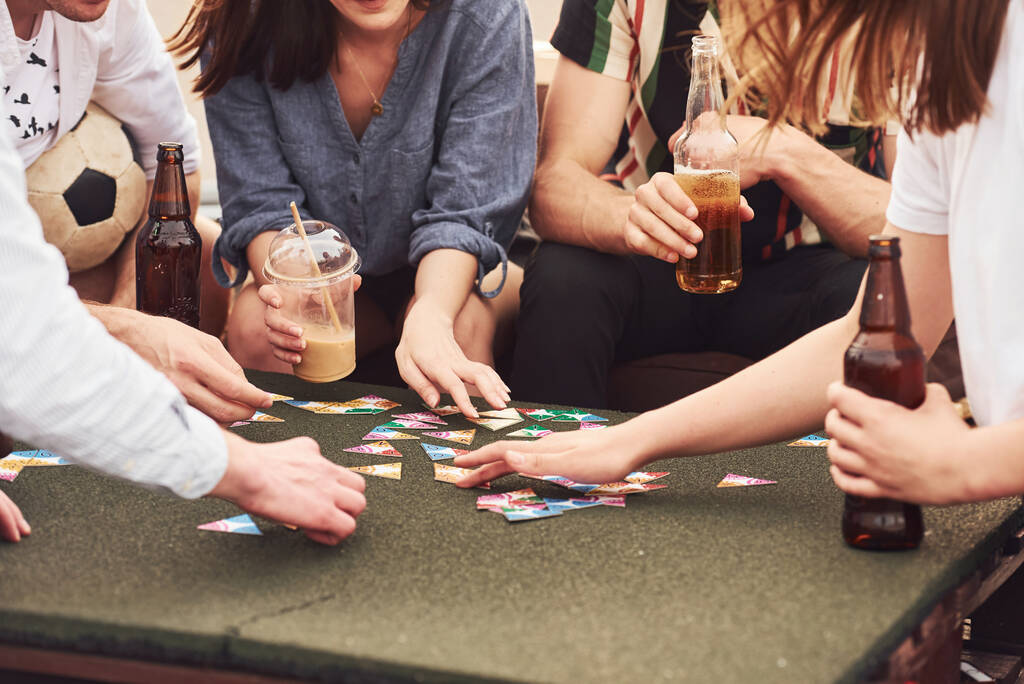 Playing game and sitting by the table. Group of young people in casual clothes have a party at rooftop together at daytime. - Photo, Image