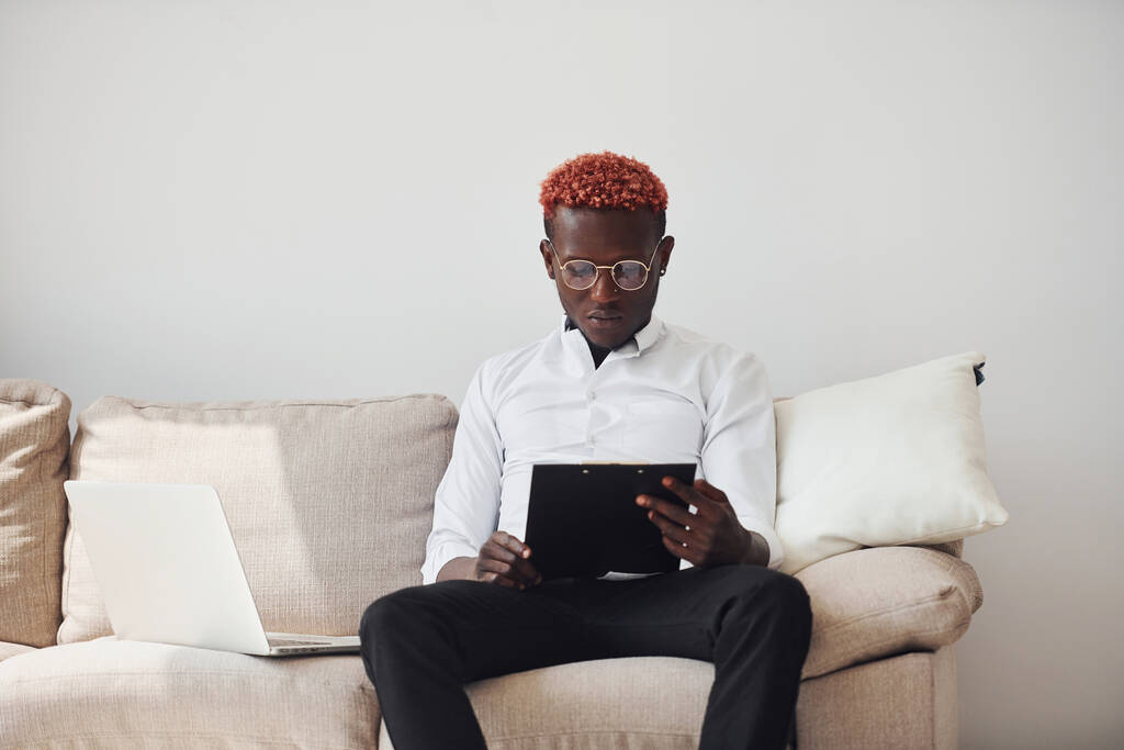 Giovane uomo afroamericano in abiti formali all'interno con computer portatile in mano. - Foto, immagini