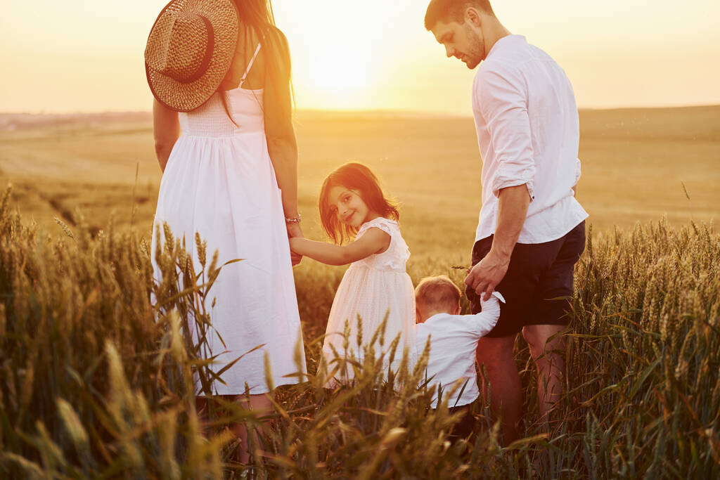 Вид ззаду. Сім'я з чотирьох чоловік проводить вільний час на полі в сонячний день під час літа
. - Фото, зображення