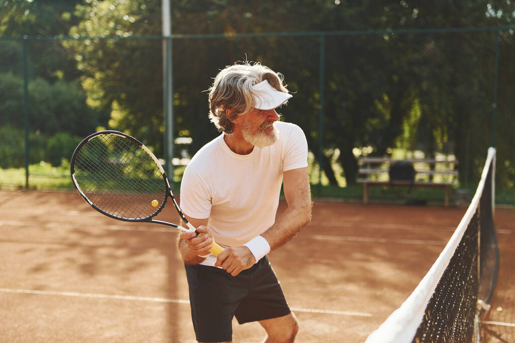 Pelataan peliä. Vanhempi moderni tyylikäs mies maila ulkona tenniskentällä päivällä. - Valokuva, kuva