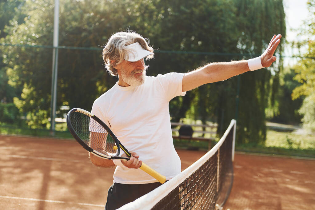 Senior uomo moderno elegante con racchetta all'aperto sul campo da tennis durante il giorno. - Foto, immagini