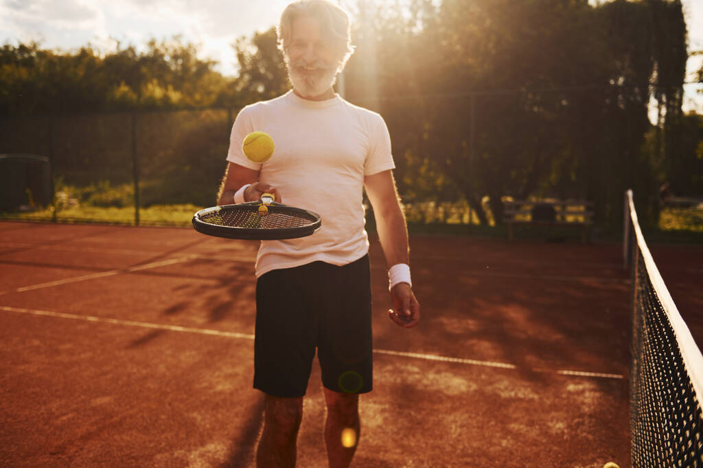 Training tijd. Senioren moderne stijlvolle man met racket buiten op de tennisbaan overdag. - Foto, afbeelding