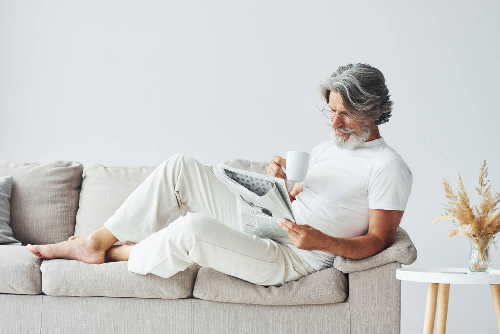 Descansando en el sofá. Senior elegante hombre moderno con pelo gris y barba en el interior. - Foto, Imagen