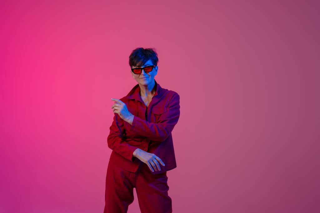 Mature european woman wearing sunglasses dancing on camera isolated over pink background - Photo, Image