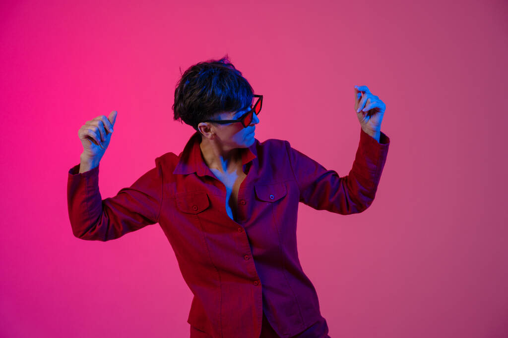 Доросла жінка з сонцезахисними окулярами танцює на фотоапараті, ізольованому над рожевим фоном. - Фото, зображення