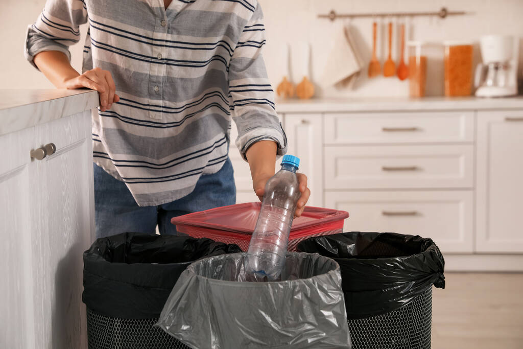 Mujer arrojando botella de plástico en el cubo de basura en la cocina, primer plano. Recogida separada de residuos - Foto, Imagen
