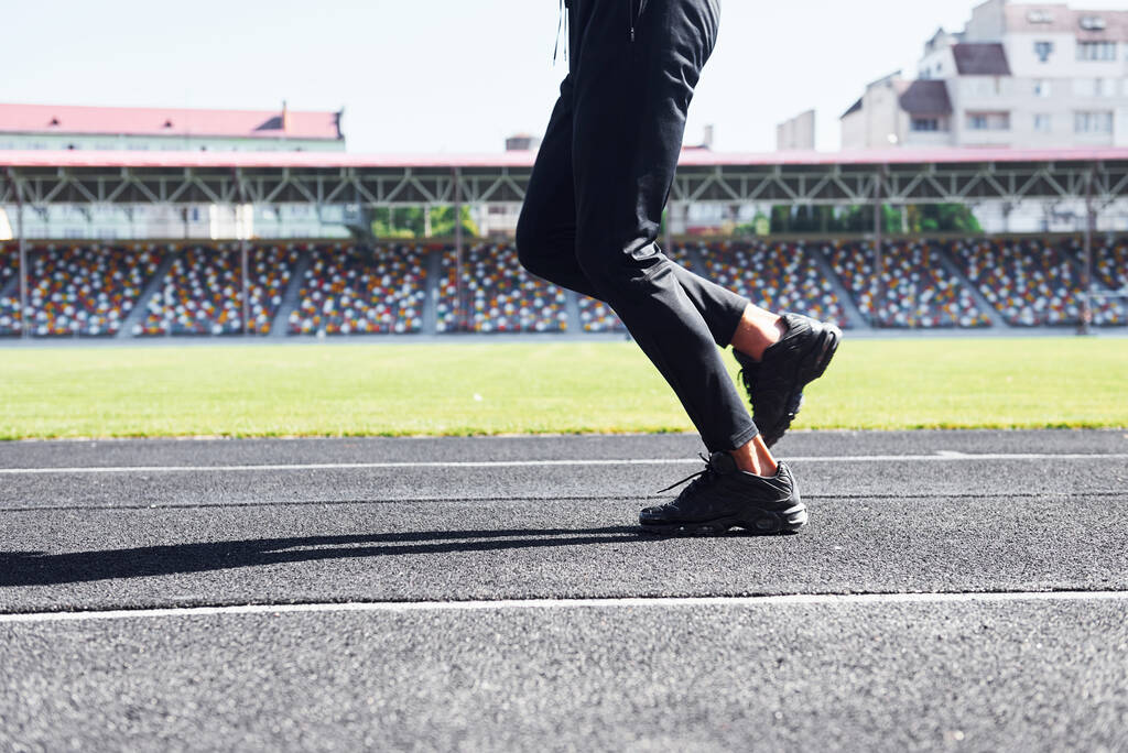 Közelkép a lábak futó fekete nadrág és cipő, hogy a szabadban a pályán. - Fotó, kép