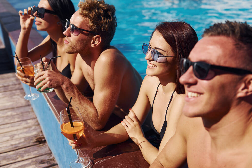 Puhumista ja juomista. Ryhmä nuoria onnellisia ihmisiä pitää hauskaa uima-altaassa päivällä. - Valokuva, kuva
