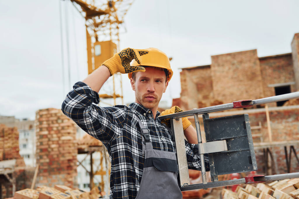 Scala in mano. Il lavoratore edile in uniforme e le attrezzature di sicurezza hanno un lavoro nell'edilizia. - Foto, immagini