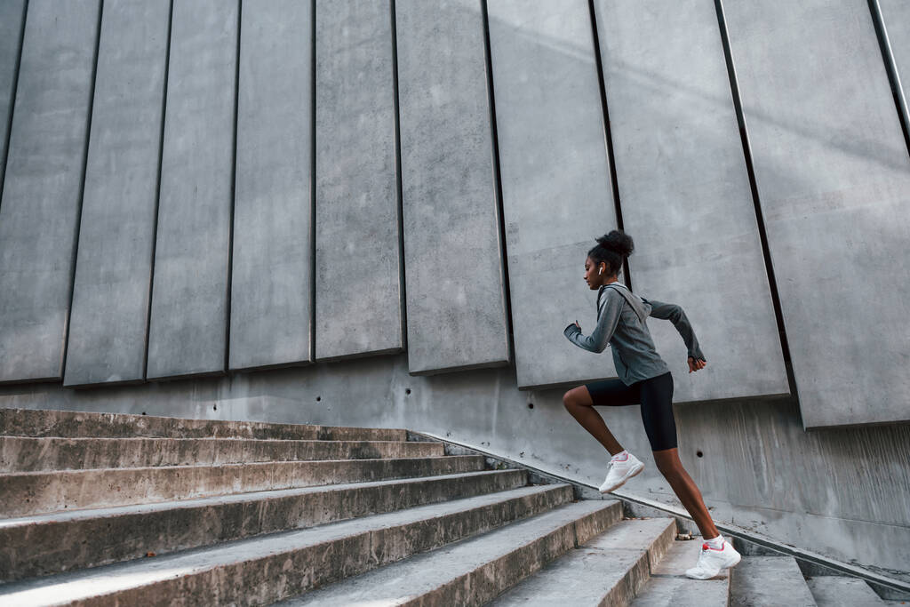Szybki biegacz. Młoda Afroamerykanka w sportowej odzieży ćwiczy na świeżym powietrzu w dzień. - Zdjęcie, obraz