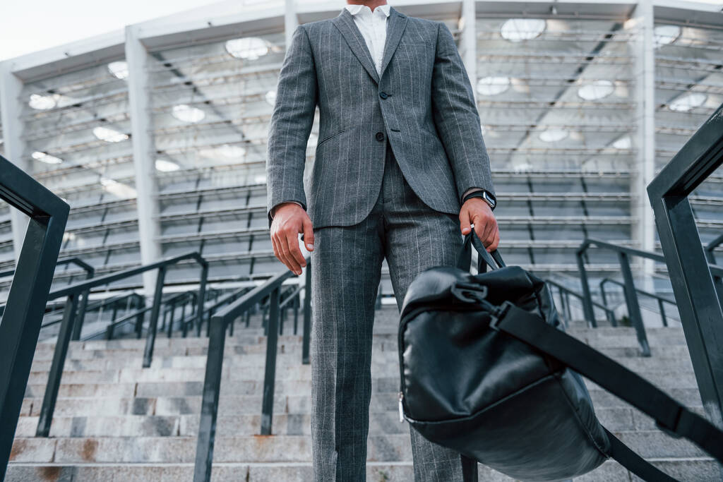 Держит сумку в руках. Молодой бизнесмен в серой формальной одежде на открытом воздухе в городе. - Фото, изображение