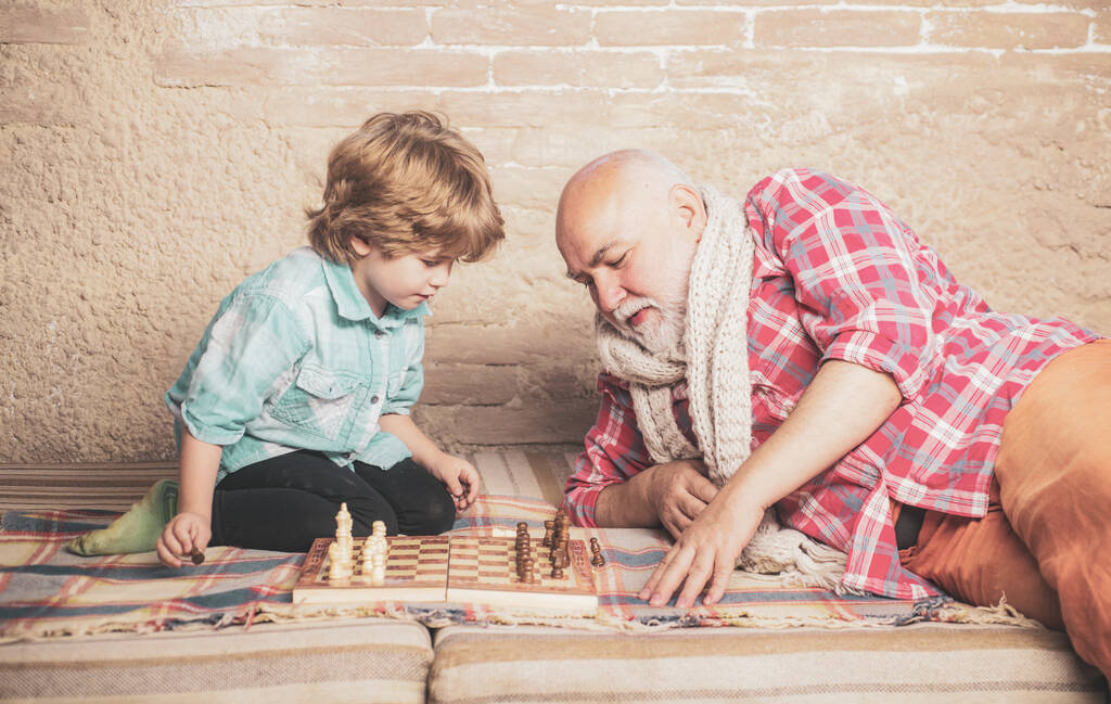 Зрелый мужчина с маленьким мальчиком играет в шахматы. Шах и мат. Милый мальчик играет в шахматы. Детство. Концепция дедушки и внука. Шахматная фигура. - Фото, изображение
