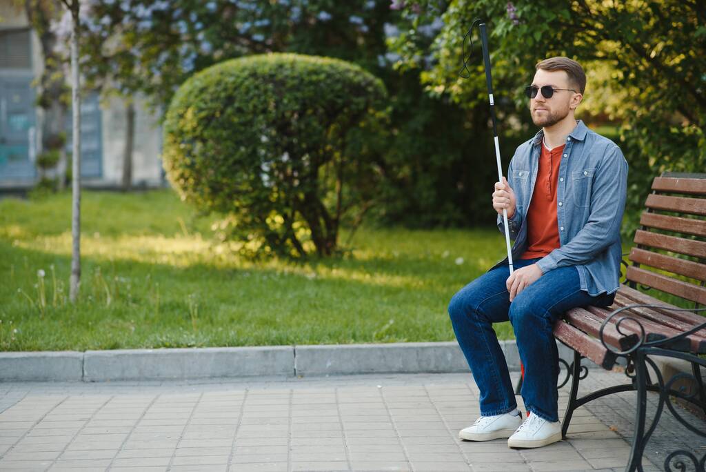 Homme malvoyant avec bâton de marche, assis sur un banc dans le parc de la ville. Espace de copie. - Photo, image