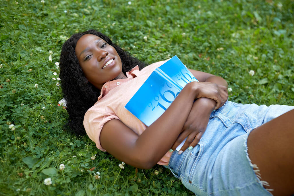 menina estudante africano com livro didático deitado na grama - Foto, Imagem
