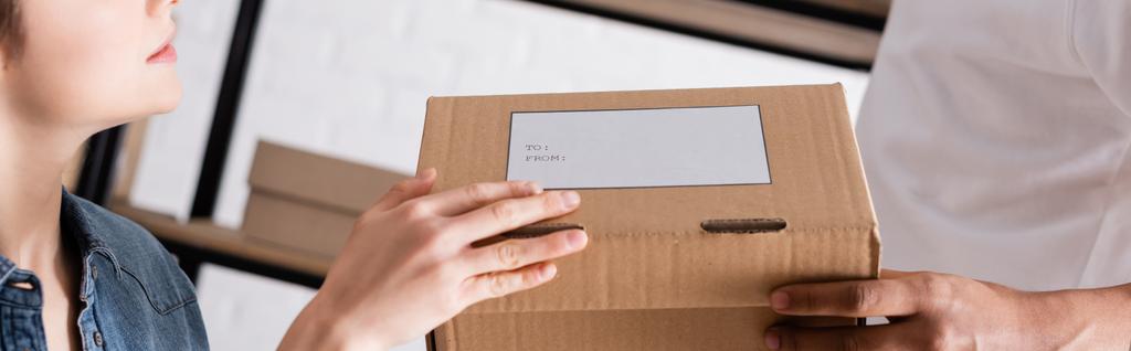 Vista recortada de vendedores interracial sosteniendo caja de cartón con etiqueta de envío en tienda web en línea, banner  - Foto, imagen
