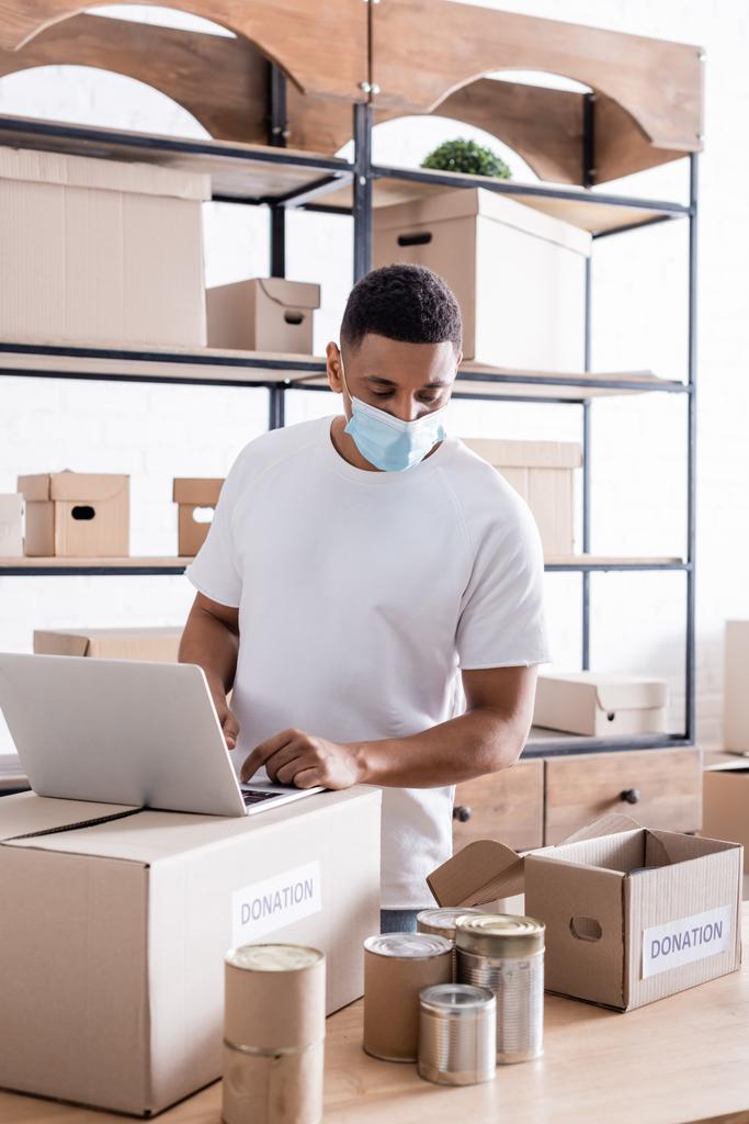 Afrikai-amerikai eladó orvosi maszk segítségével laptop közelében dobozok és adomány doboz online áruház  - Fotó, kép