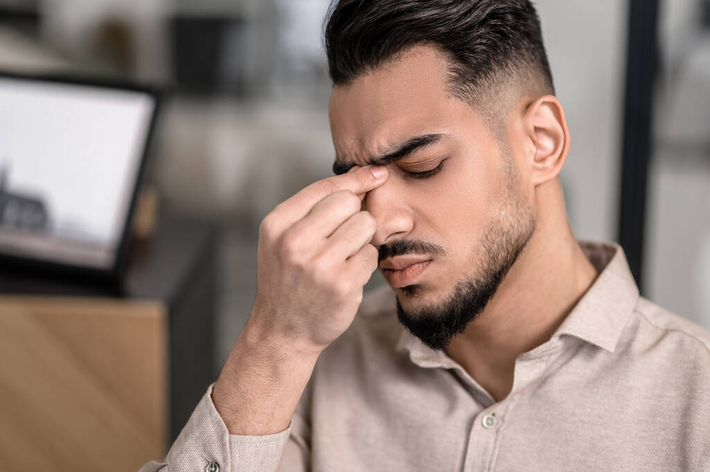 Ein dunkelhaariger Mann berührt seinen Nasenrücken und hat Kopfschmerzen - Foto, Bild