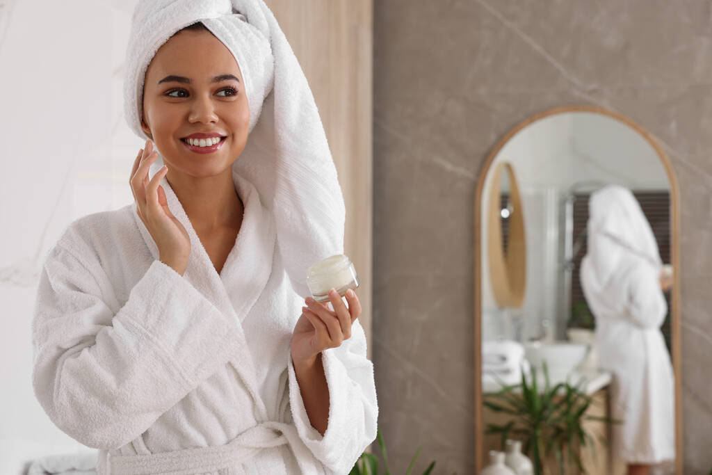 Hermosa mujer afroamericana aplicando crema en la cara en el baño, espacio para el texto - Foto, imagen