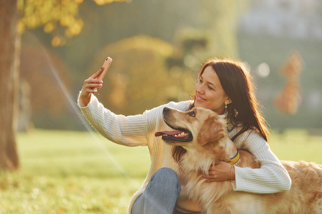Haciendo selfie. Mujer joven dar un paseo con Golden Retriever en el parque. - Foto, Imagen