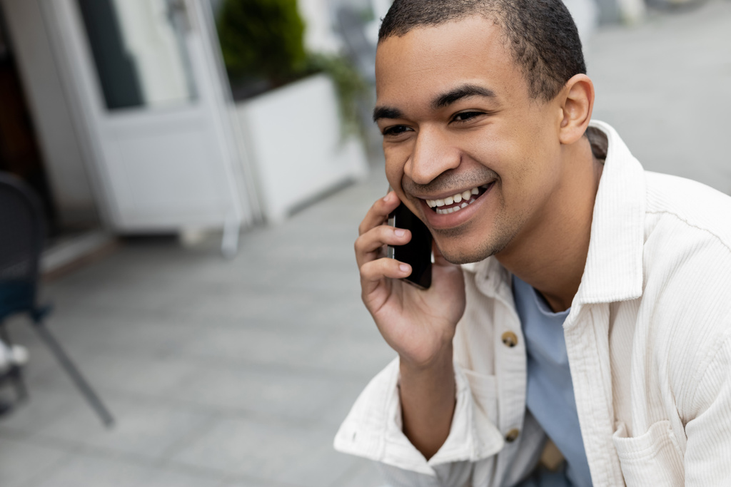 щасливий афроамериканський чоловік говорить на смартфоні на літній терасі
  - Фото, зображення